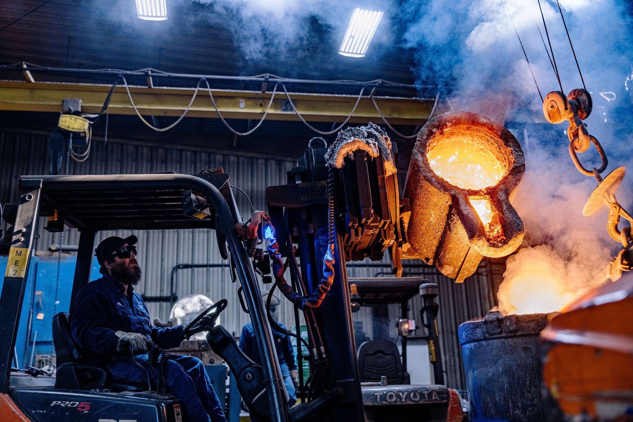 Ladle pouring molten alloy into a printed sand mold at an independent US foundry, no hard tooling on the pour.